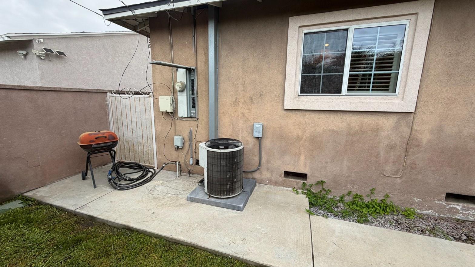 Old AC condenser unit on concrete pad beside stucco house in Norwalk before HVAC system replacement