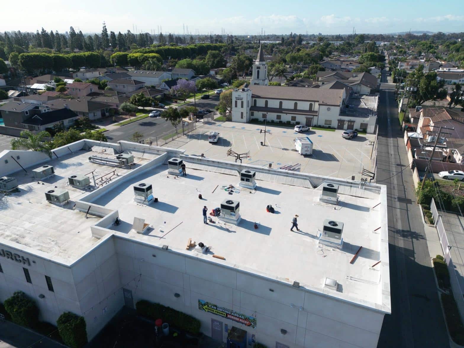 Workers installing packaged rooftop HVAC units on a white TPO commercial flat roof in Paramount CA